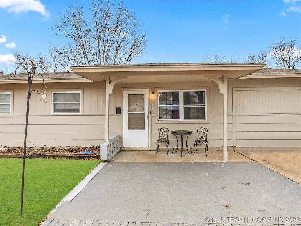 entrance to property featuring a garage, a patio, and a lawn