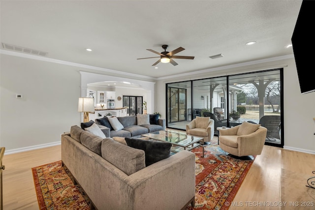 living room with ceiling fan, ornamental molding, light hardwood / wood-style floors, and a textured ceiling