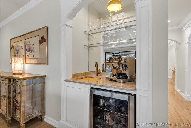 bar featuring wine cooler, light wood-type flooring, ornamental molding, and ornate columns