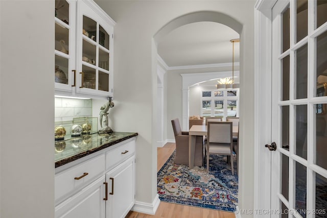 interior space with white cabinetry, crown molding, dark stone countertops, light hardwood / wood-style floors, and backsplash