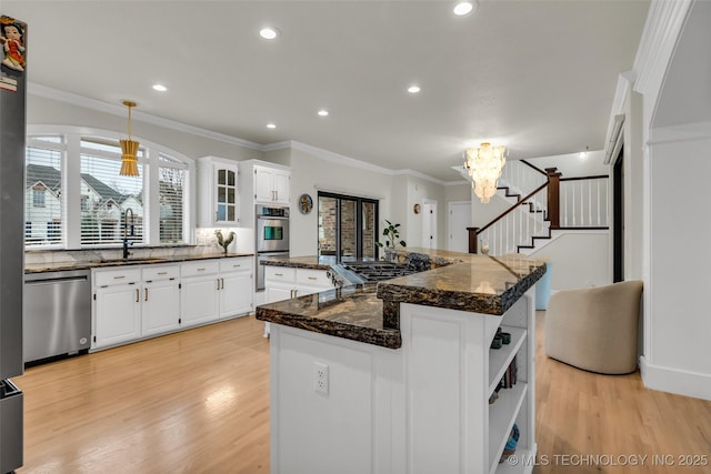 kitchen with stainless steel appliances, a sink, white cabinets, light wood finished floors, and crown molding