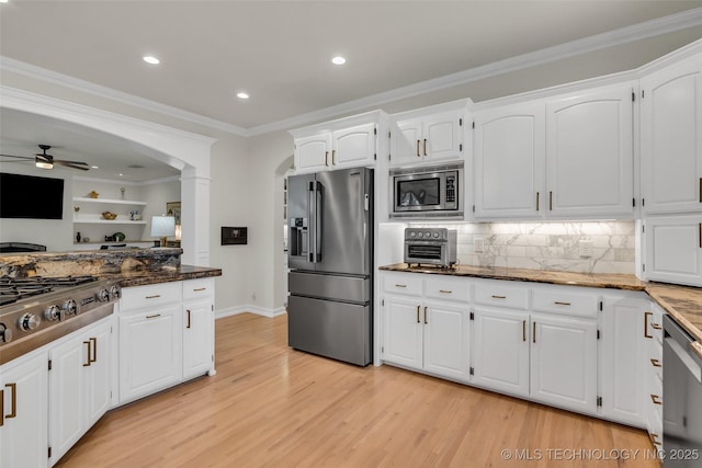 kitchen with light wood-style flooring, appliances with stainless steel finishes, ornamental molding, dark stone countertops, and white cabinetry