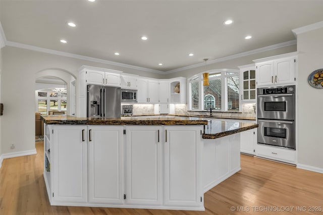 kitchen with arched walkways, appliances with stainless steel finishes, plenty of natural light, and a kitchen island