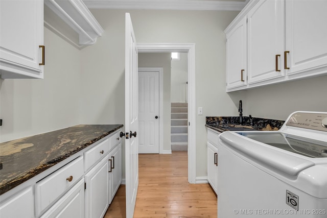 laundry area with a sink, baseboards, light wood-type flooring, cabinet space, and washer / dryer