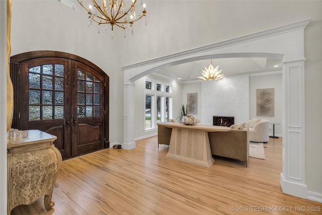 foyer entrance with light hardwood / wood-style flooring, a chandelier, ornamental molding, a premium fireplace, and french doors