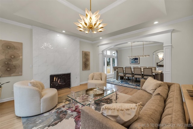 living room with arched walkways, a tile fireplace, wood finished floors, ornamental molding, and an inviting chandelier