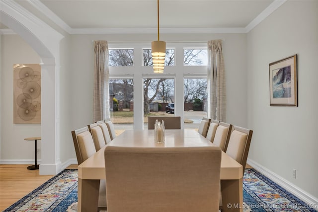 dining area featuring arched walkways, ornamental molding, wood finished floors, and baseboards