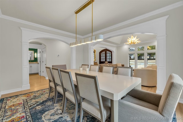 dining area featuring an inviting chandelier, light wood-type flooring, ornamental molding, and ornate columns