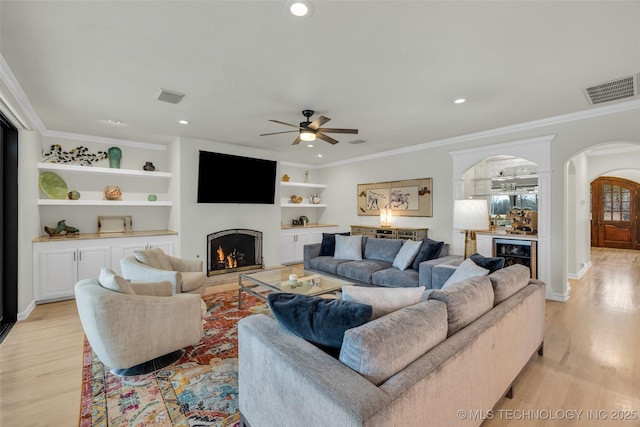 living room featuring wine cooler, ornamental molding, light hardwood / wood-style floors, bar area, and built in shelves