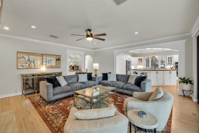 living room with ceiling fan, ornamental molding, sink, and light hardwood / wood-style flooring