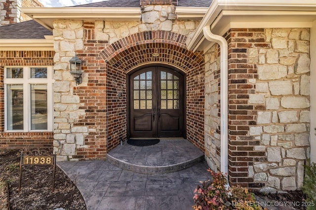 entrance to property featuring french doors, roof with shingles, and brick siding