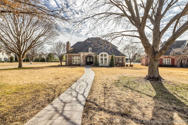 french country inspired facade featuring french doors, brick siding, a chimney, and a front lawn