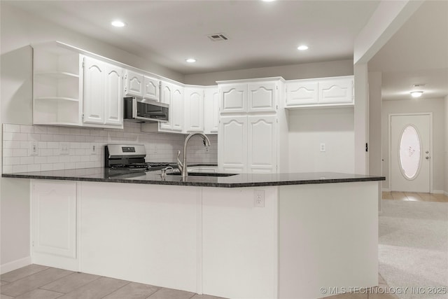 kitchen featuring sink, appliances with stainless steel finishes, kitchen peninsula, dark stone counters, and white cabinets