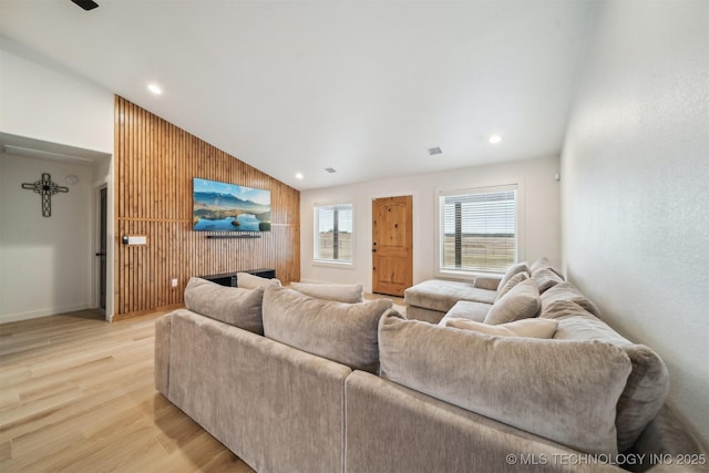 living room with light hardwood / wood-style flooring, a fireplace, vaulted ceiling, and wooden walls