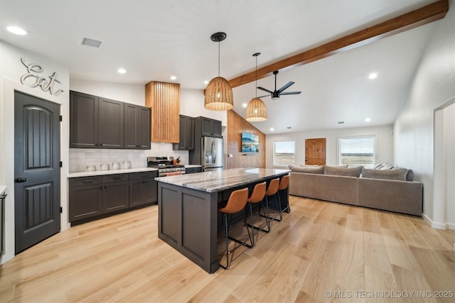 kitchen featuring a kitchen bar, hanging light fixtures, appliances with stainless steel finishes, beam ceiling, and light stone countertops