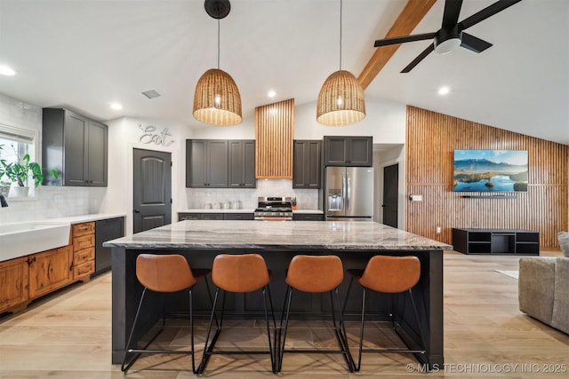 kitchen featuring appliances with stainless steel finishes, pendant lighting, sink, a breakfast bar area, and light stone counters