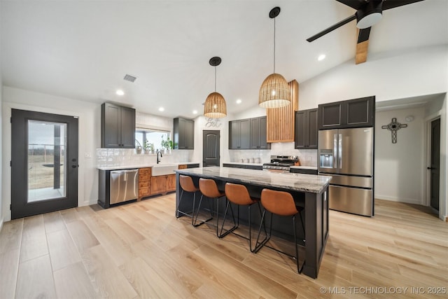 kitchen with appliances with stainless steel finishes, pendant lighting, lofted ceiling with beams, a center island, and light stone countertops