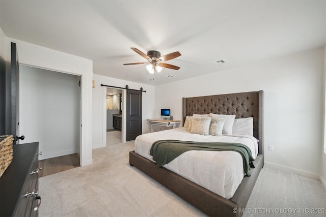 bedroom with ceiling fan, light colored carpet, connected bathroom, and a barn door