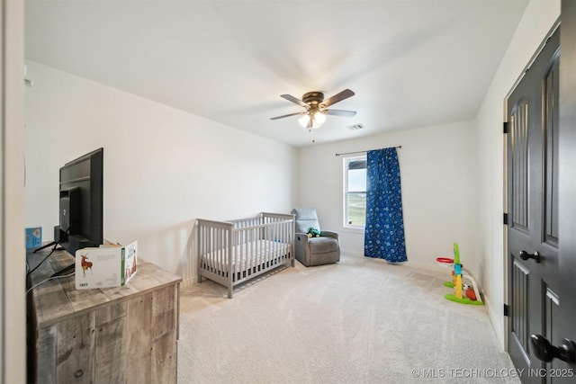 carpeted bedroom with a crib and ceiling fan