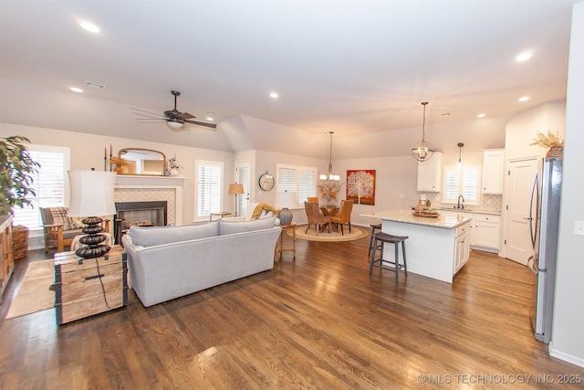 living room with sink, vaulted ceiling, dark hardwood / wood-style flooring, a tiled fireplace, and ceiling fan with notable chandelier