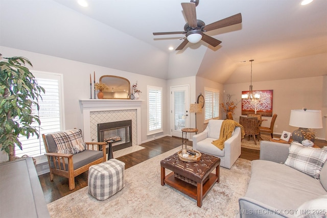 living room with lofted ceiling, ceiling fan with notable chandelier, wood-type flooring, and a tile fireplace