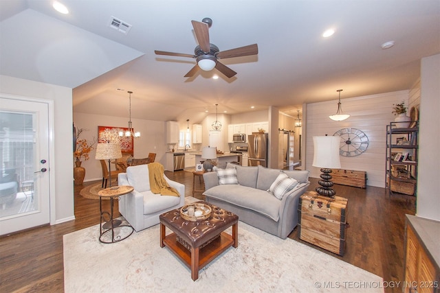 living room with ceiling fan with notable chandelier, wooden walls, wood-type flooring, lofted ceiling, and sink