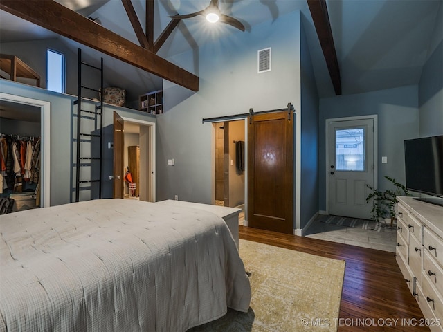 bedroom with dark hardwood / wood-style floors, a barn door, a walk in closet, a closet, and beamed ceiling