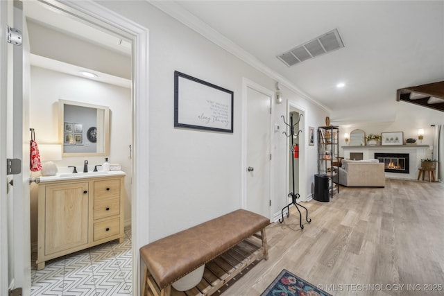 hallway featuring sink, crown molding, and light wood-type flooring