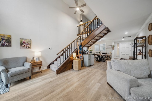 living room with crown molding, a towering ceiling, light hardwood / wood-style floors, and ceiling fan