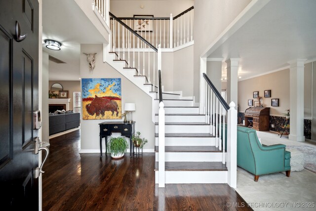 foyer featuring ornamental molding, wood-type flooring, decorative columns, and a high ceiling