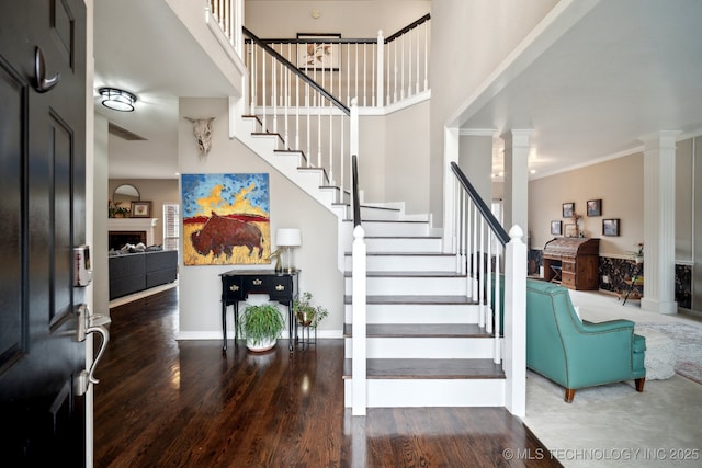 entryway with hardwood / wood-style floors, crown molding, decorative columns, and a towering ceiling