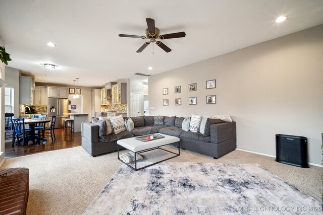 carpeted living room featuring ceiling fan and sink