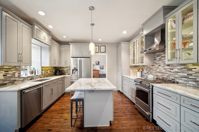 kitchen with pendant lighting, sink, premium appliances, a center island, and wall chimney range hood