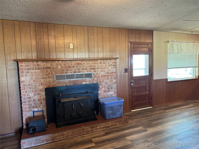 unfurnished living room with dark wood-type flooring, wooden walls, a fireplace, and a textured ceiling