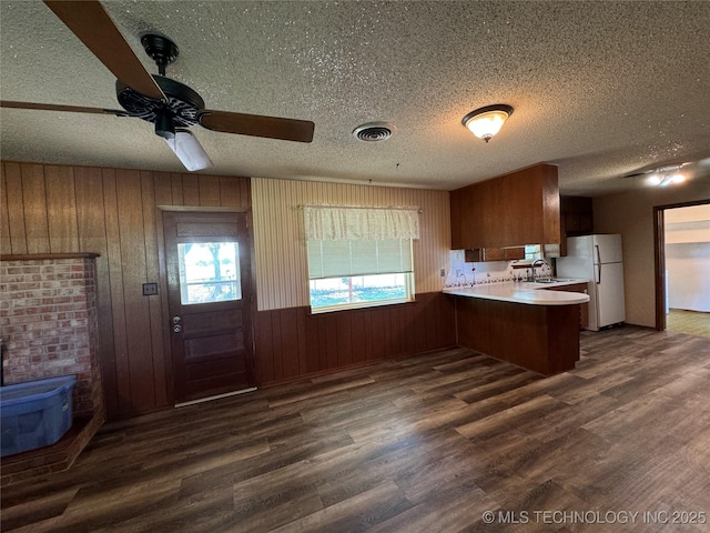 kitchen with dark wood-type flooring, sink, a wood stove, white refrigerator, and kitchen peninsula