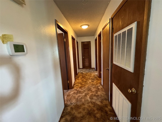 hallway featuring a textured ceiling and dark colored carpet