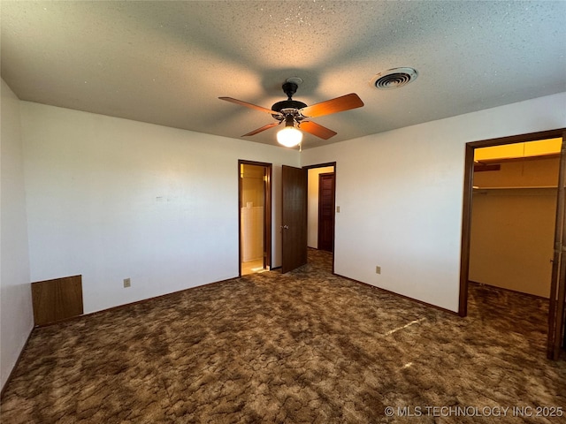 unfurnished bedroom with dark colored carpet, a walk in closet, ceiling fan, a textured ceiling, and a closet