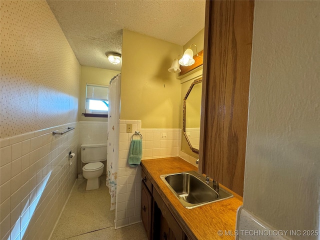 bathroom featuring vanity, toilet, a textured ceiling, and tile walls