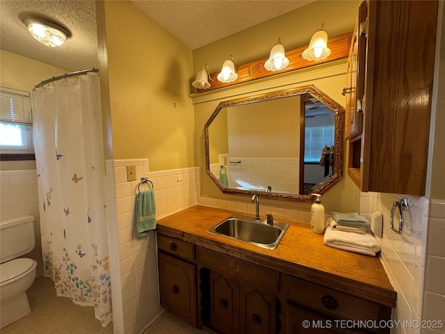 bathroom featuring tile walls, vanity, toilet, and a textured ceiling