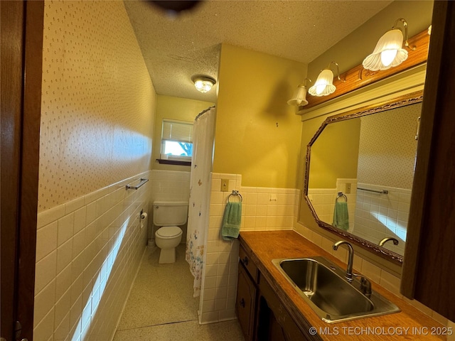 bathroom featuring vanity, toilet, a textured ceiling, and tile walls