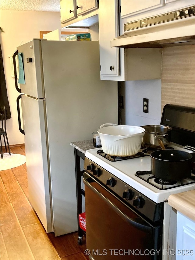 kitchen with white cabinetry, a textured ceiling, white appliances, and light hardwood / wood-style floors