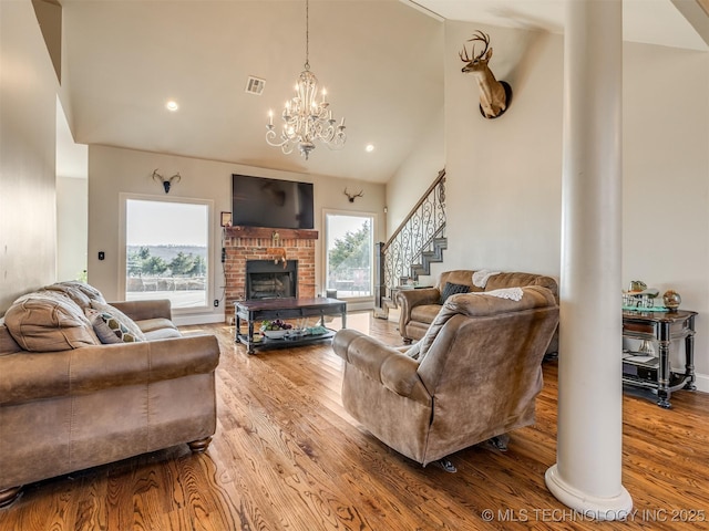 living room featuring hardwood / wood-style flooring, high vaulted ceiling, a brick fireplace, and a notable chandelier