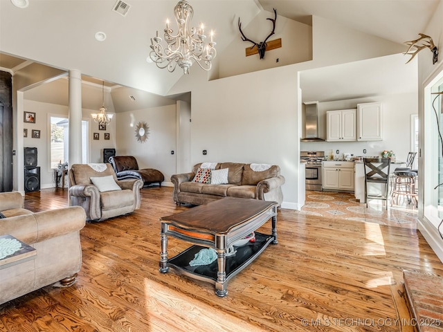 living room with decorative columns, high vaulted ceiling, an inviting chandelier, and light hardwood / wood-style floors