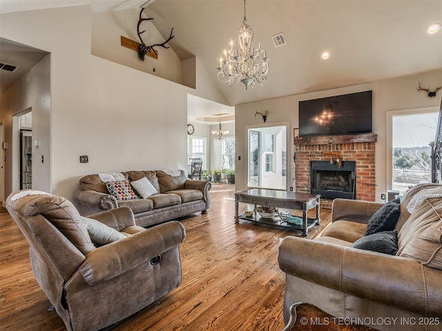 living room featuring an inviting chandelier, a healthy amount of sunlight, light hardwood / wood-style floors, and a brick fireplace