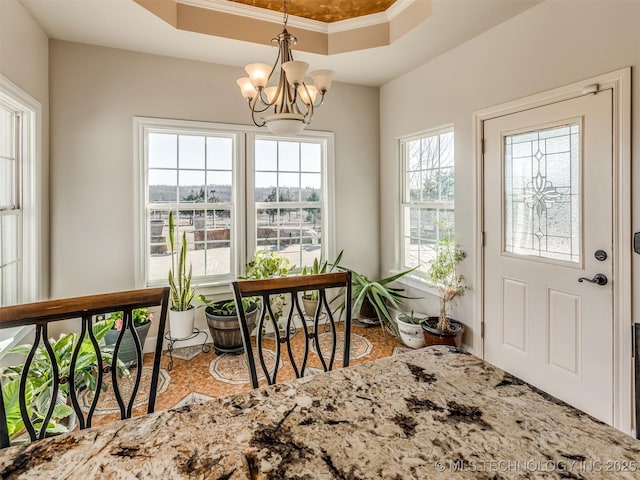 entryway featuring a notable chandelier, ornamental molding, and a raised ceiling