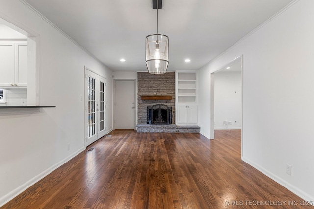 unfurnished living room with dark hardwood / wood-style flooring, a stone fireplace, crown molding, and built in shelves