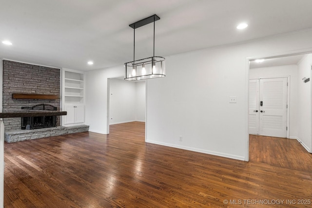 unfurnished living room with dark wood-type flooring, a large fireplace, ornamental molding, and built in shelves