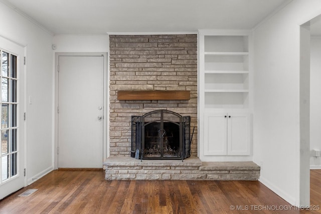 unfurnished living room featuring crown molding, dark wood-type flooring, a fireplace, and built in shelves