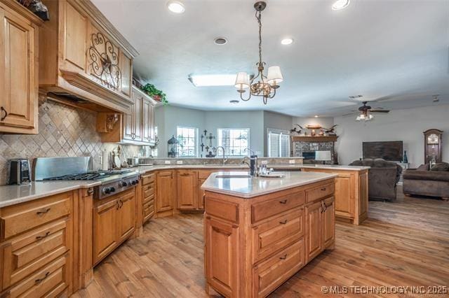 kitchen with pendant lighting, light hardwood / wood-style floors, an island with sink, and stainless steel gas stovetop