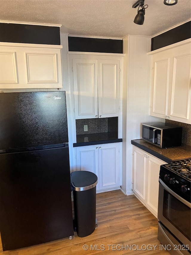 kitchen with stainless steel gas range, white cabinetry, a textured ceiling, black fridge, and light wood-type flooring